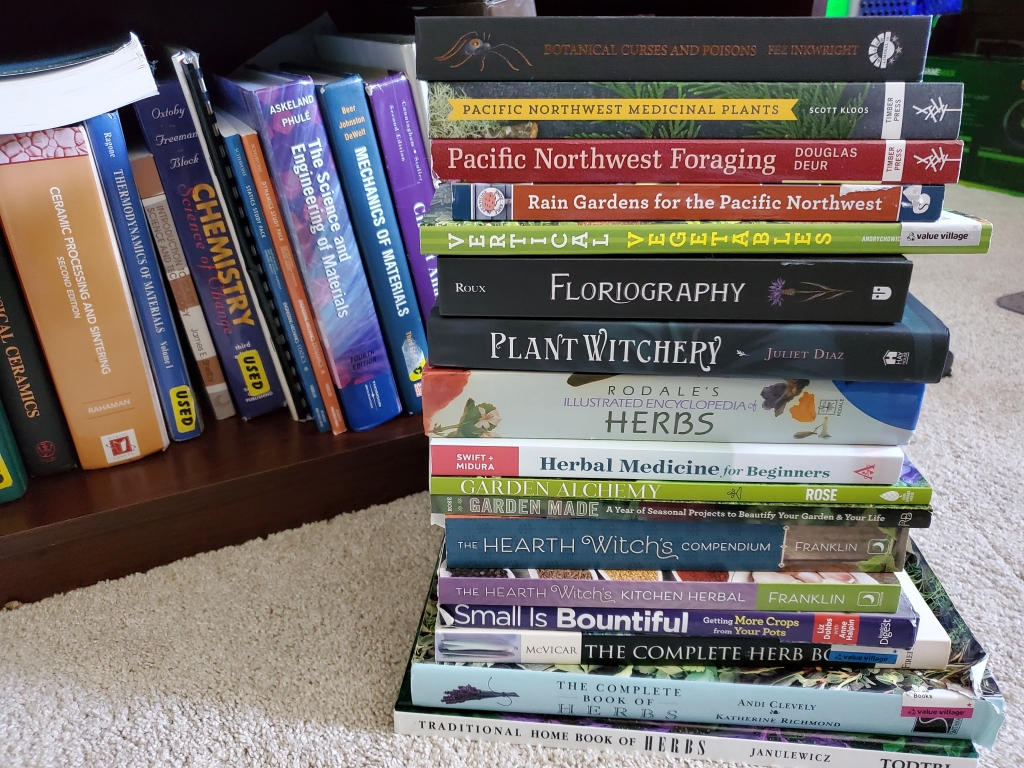 A stack of books about plants and gardening sits on the carpet in front of a bookshelf. On the bookshelf are old college materials science textbooks.